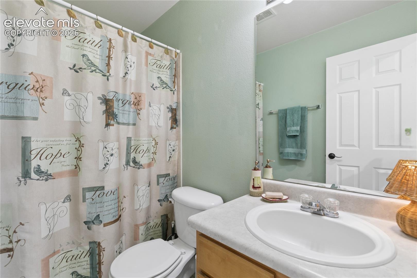White paneled door, light wood-finish vanity, integrated sink, wall-mounted mirror, and overhead vanity lighting
