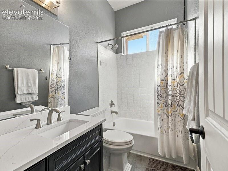 Vanity with white integrated sink and brushed nickel fixtures, black cabinetry, full-width wall mirror, white tiled shower and tub combination, and an upper window
