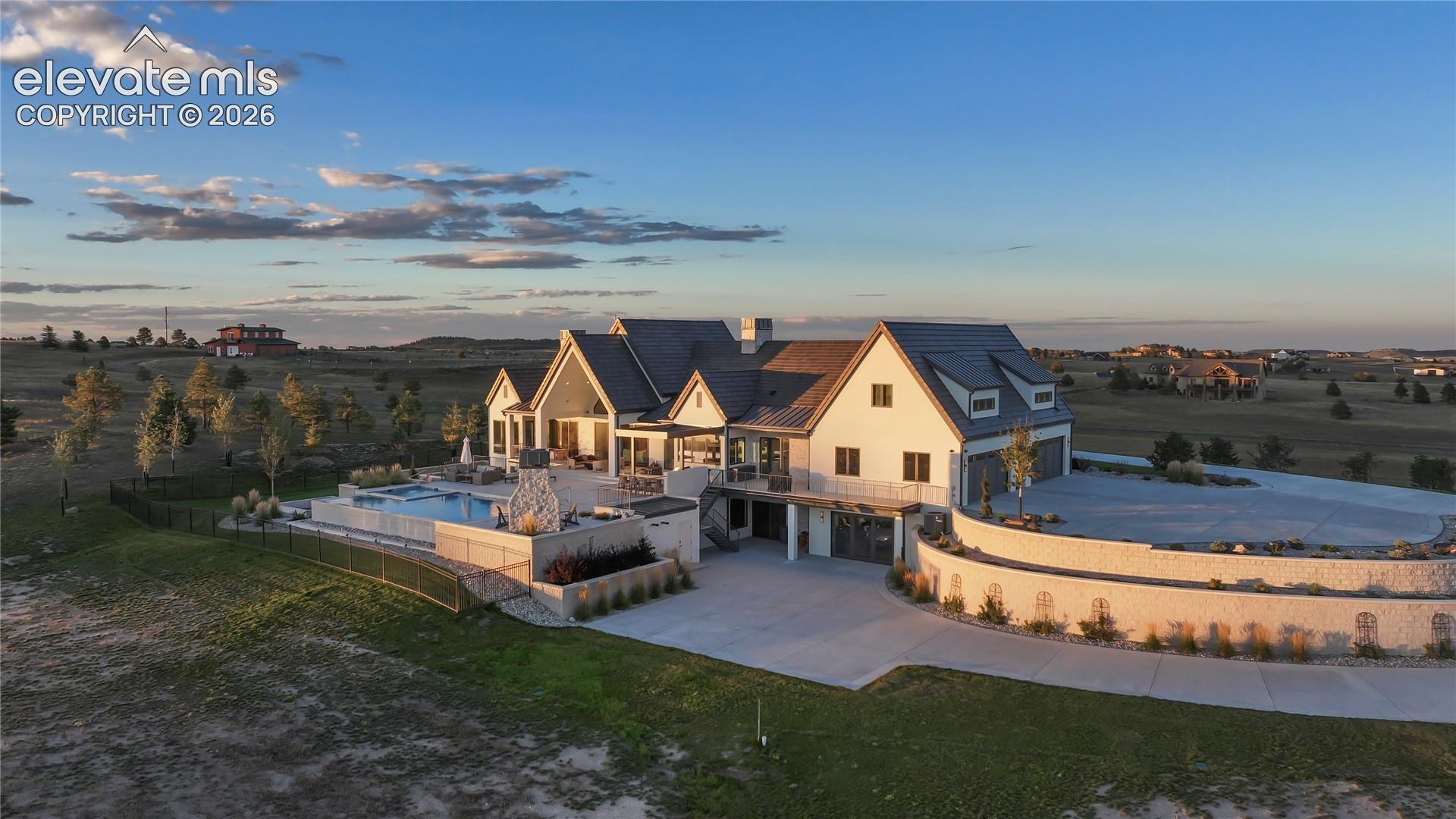 Multi-gabled estate featuring a concrete driveway, retaining walls with stone detailing, an integrated swimming pool, and a metal roof