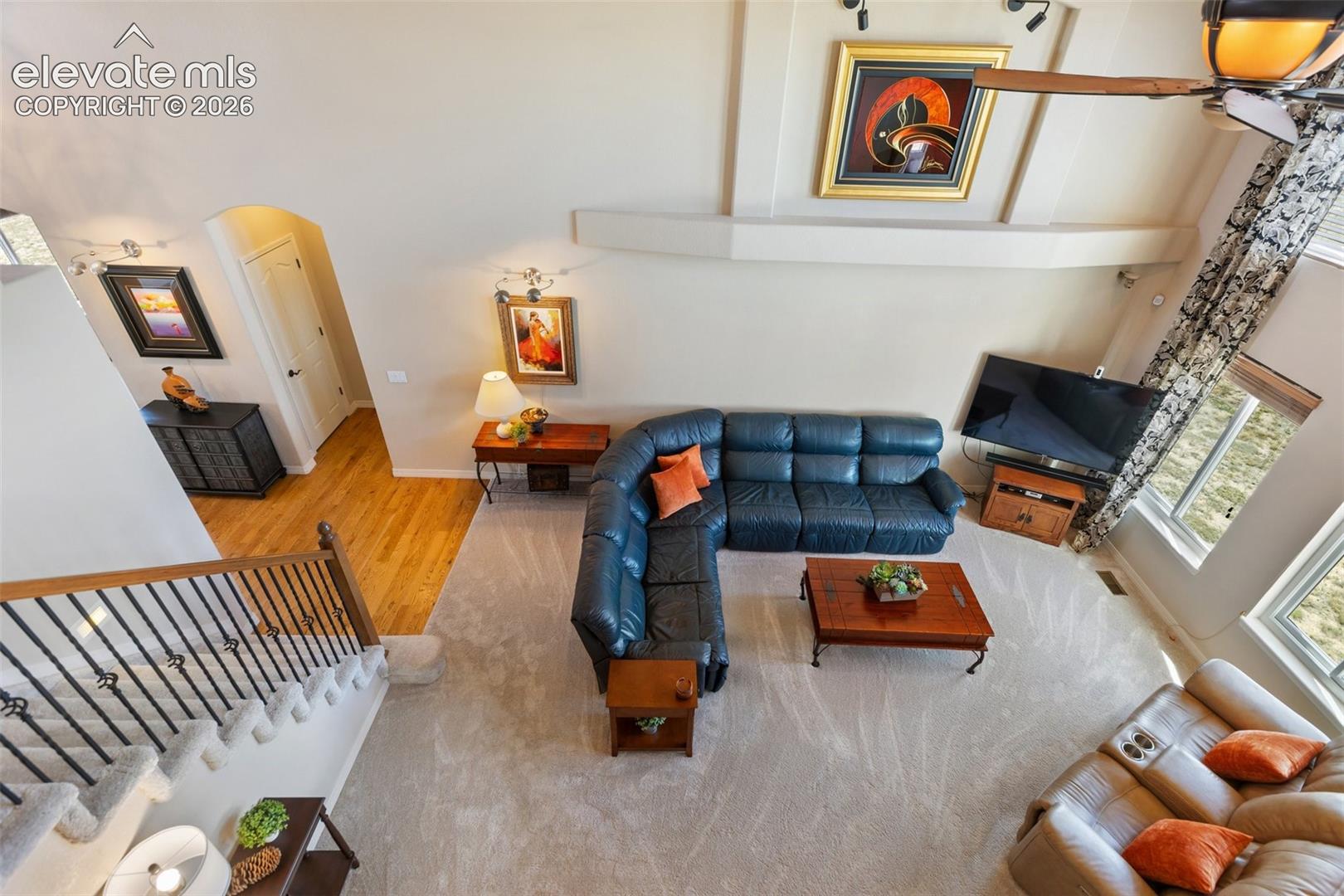 High-ceilinged living area featuring a decorative built-in wall niche, wrought-iron staircase railing, wood-finish flooring, and expansive windows