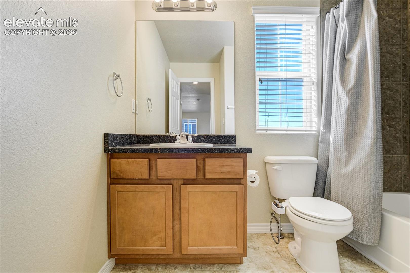 Vanity with a dark countertop and a white basin sink, wood-finish cabinetry, and a framed mirror
