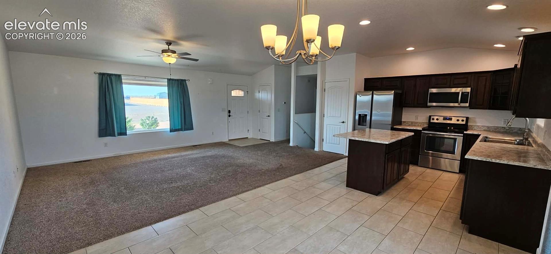 Open floor plan featuring tile flooring, dark-finish cabinetry, a central kitchen island, recessed lighting, and a multi-arm chandelier