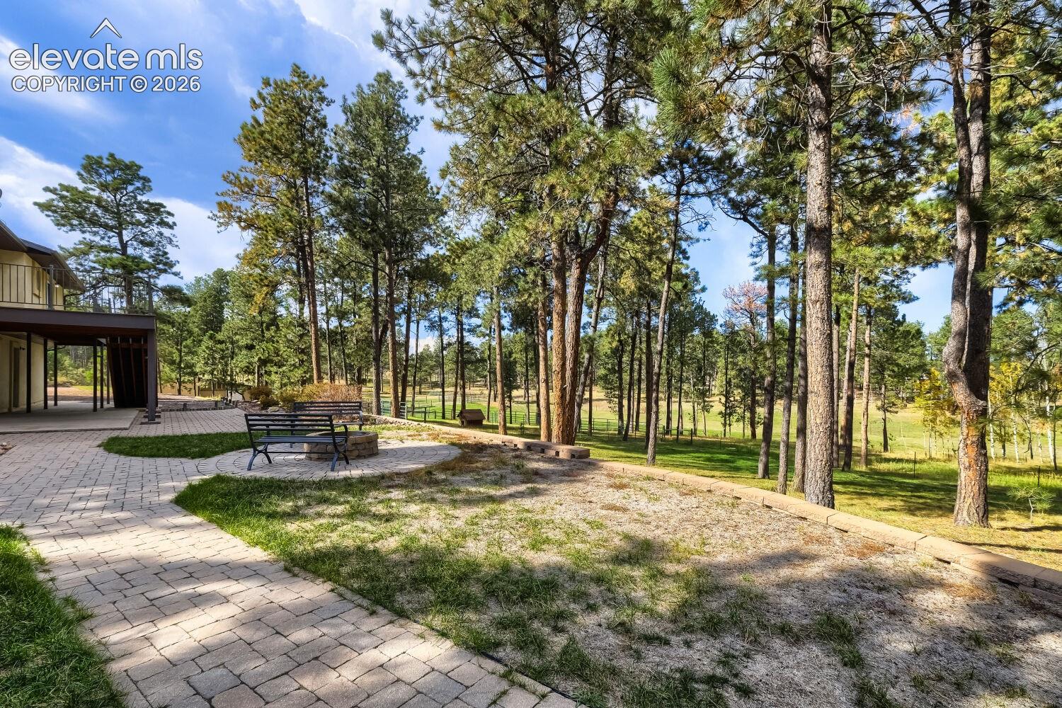 Extensive paver patio with a built-in fire pit, surrounded by mature trees and natural landscaping