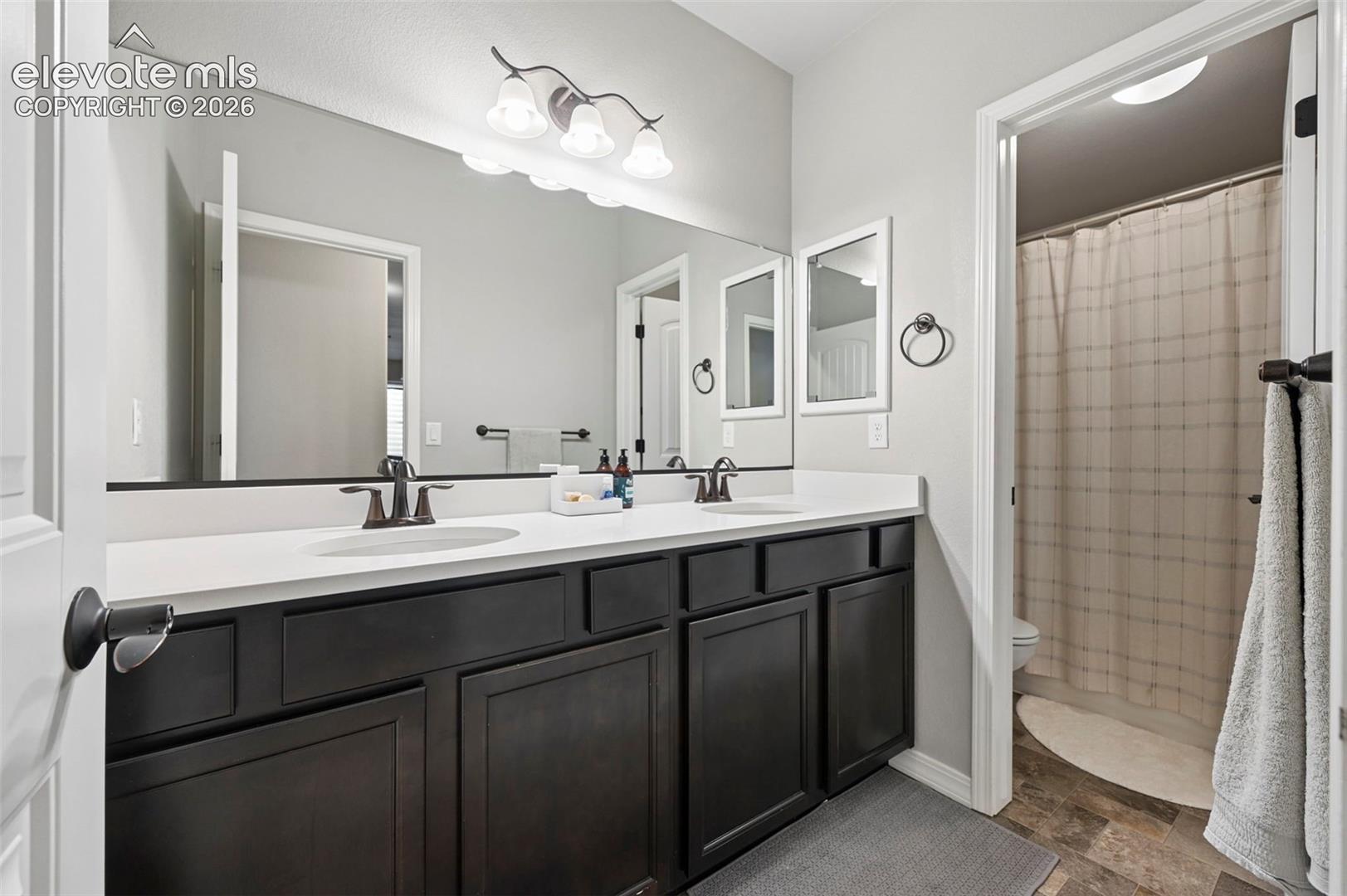 Dual-sink vanity with dark-finish cabinetry, quartz countertop, full-width wall mirror, and oil-rubbed bronze fixtures