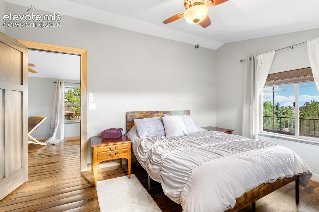 Light wood-finish flooring, a ceiling fan with integrated lighting, and a large window with white curtains