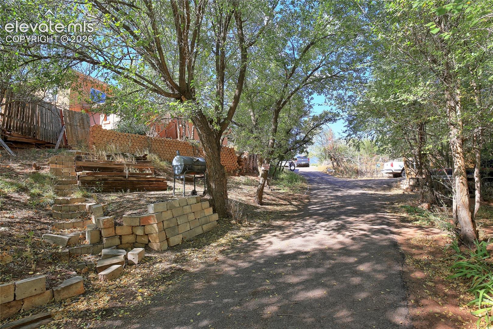 Asphalt driveway surrounded by mature trees featuring segmented stone retaining walls and timber terracing