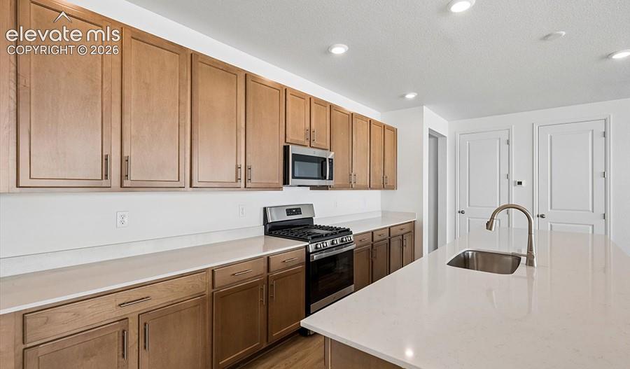 Kitchen featuring light-finish wood cabinetry, a central island with a stainless steel undermount sink, stone-finish countertops, and built-in stainless steel appliances