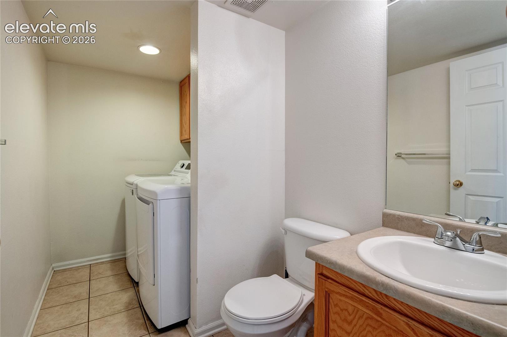 Functional utility area featuring a toilet, a single vanity with a laminate countertop, and a laundry alcove with tiled flooring
