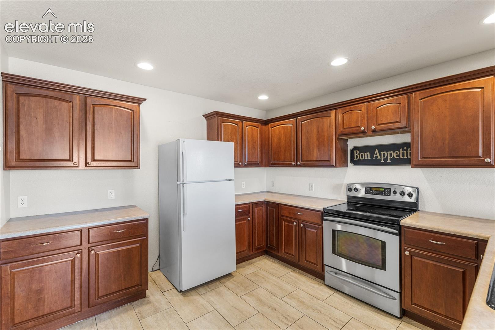 Kitchen featuring wood cabinetry, stainless steel appliances, neutral countertops, recessed lighting, and tile flooring