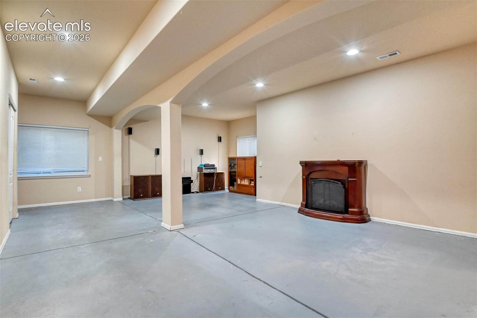 Spacious interior featuring a fireplace with a wood-finish mantel, recessed lighting, arched structural pillars, and solid-surface flooring