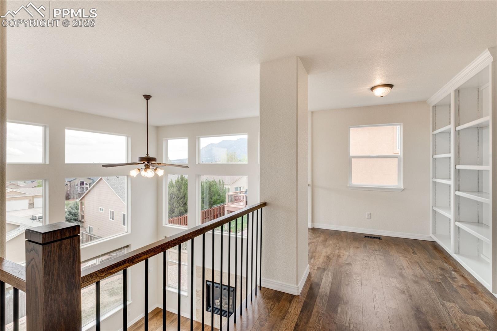 Upper-level loft landing featuring wood-finish flooring and integrated built-in shelving over-looking family room below.  