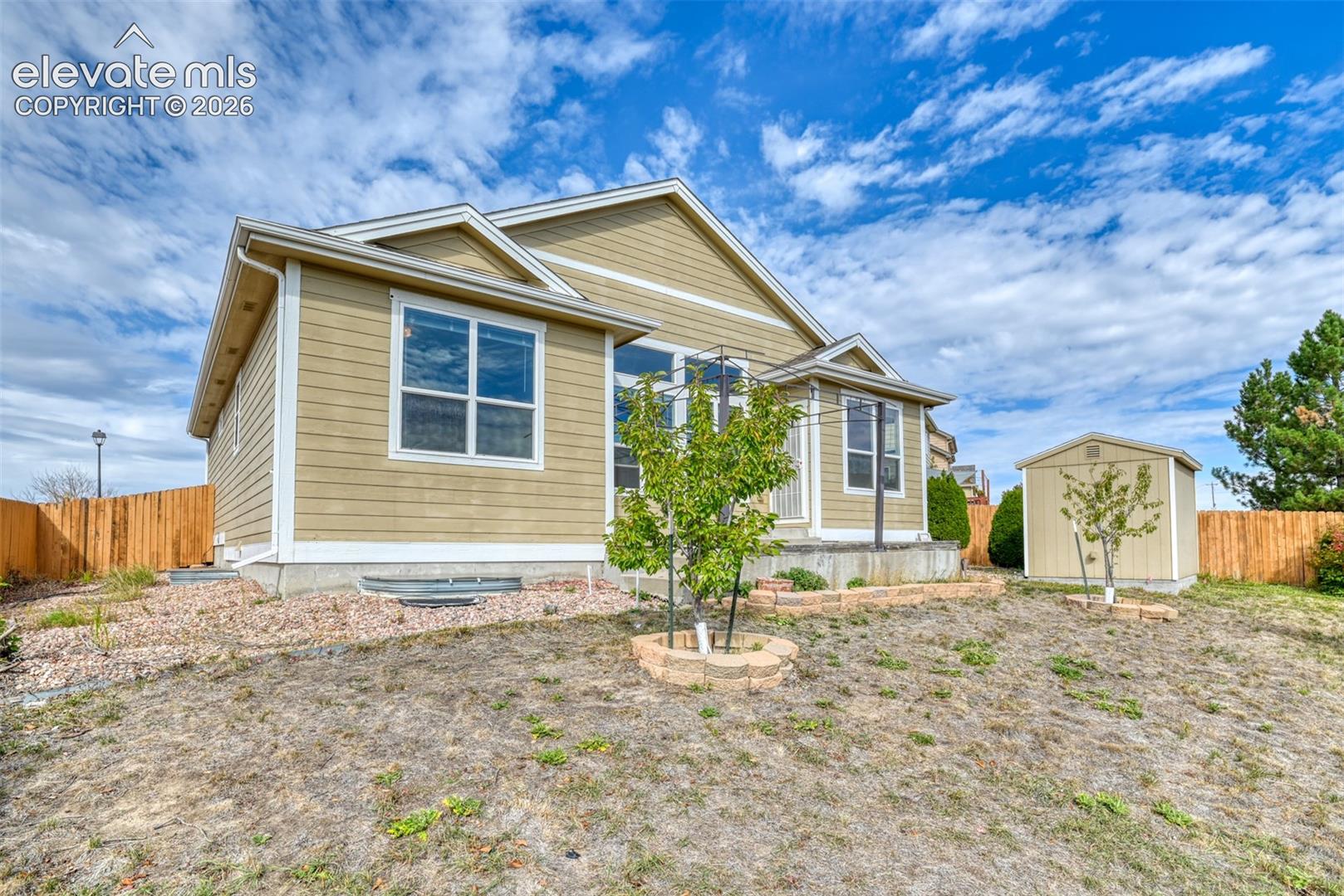 Exterior featuring horizontal lap siding, a concrete foundation, a detached storage structure, stone-paver raised garden beds, and wood-paneled fencing