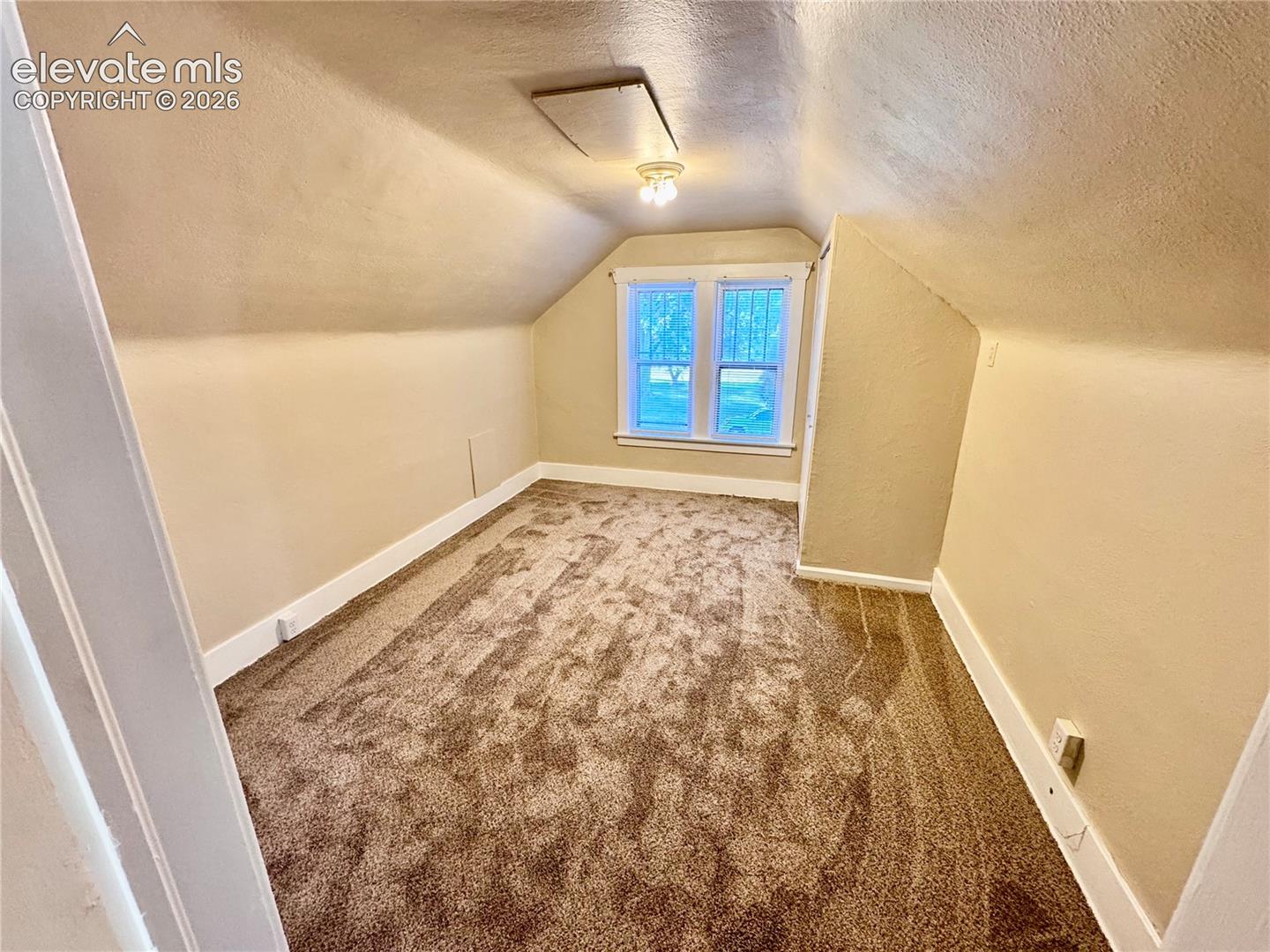 Sloped ceilings, window with white trim, recessed access panel, and brown textured carpeting