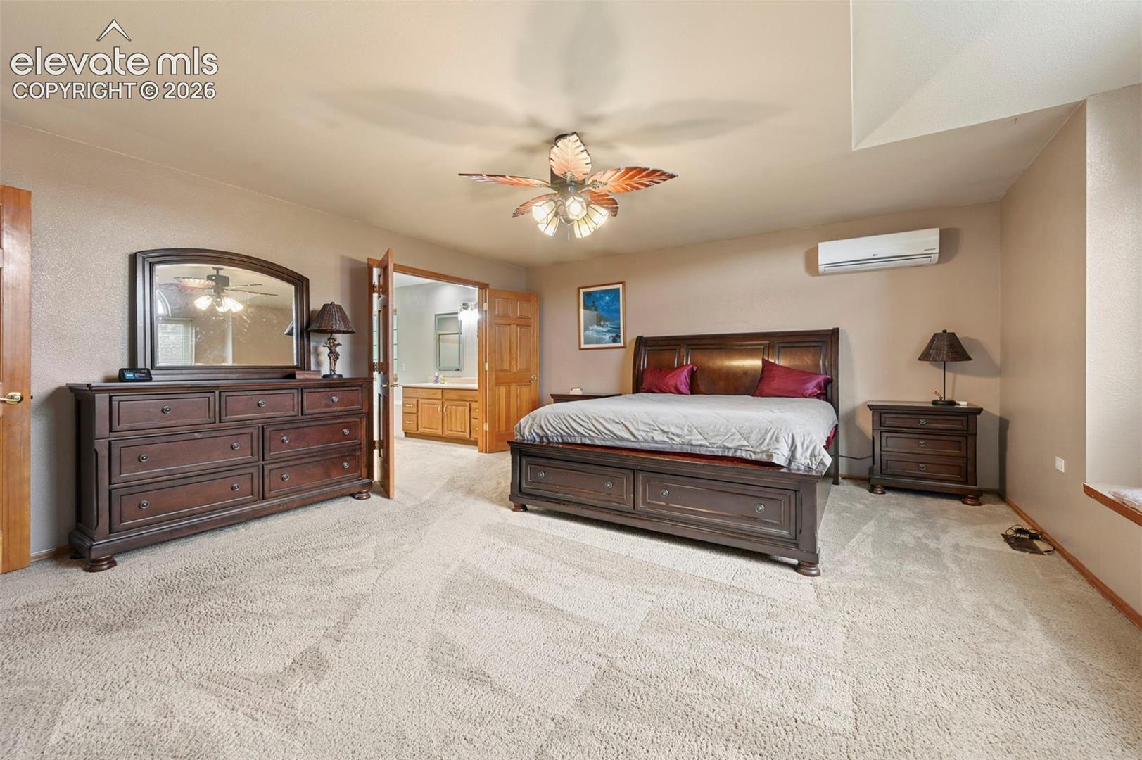 Primary bedroom with ceiling fan, arched window, window bench, wall-mounted climate control unit, and carpeted flooring