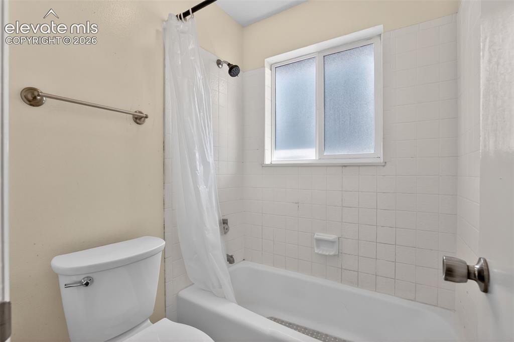 Bathroom featuring a shower-tub combination, white ceramic tile surround, and a frosted window