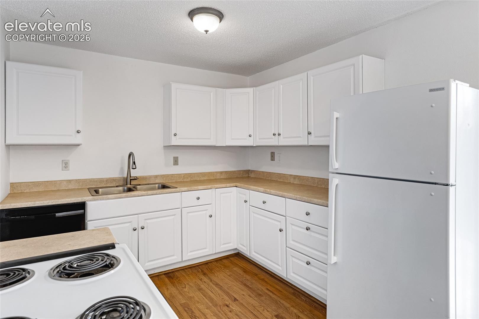 Bright, efficient kitchen featuring white cabinetry with ample storage, wood-finish countertops, stainless steel sink with faucet, electric coil cooktop, and white refrigerator