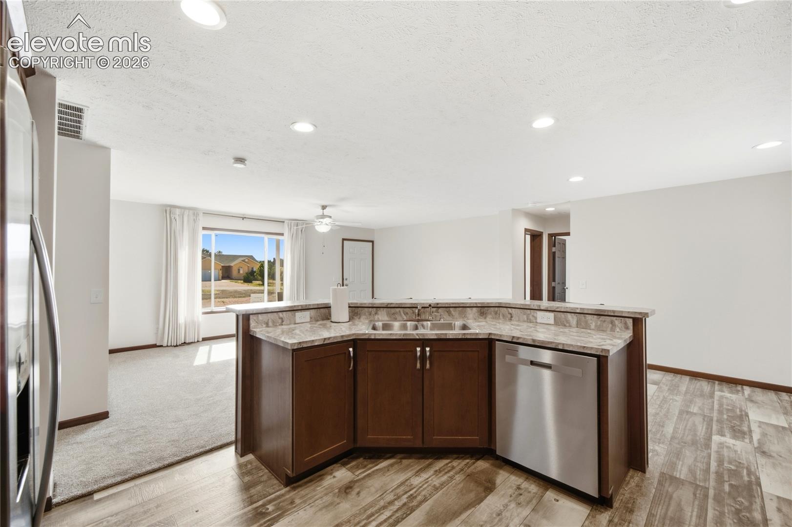 Open-concept kitchen island featuring rich wood cabinetry with stainless steel appliances, granite countertops, and recessed lighting throughout