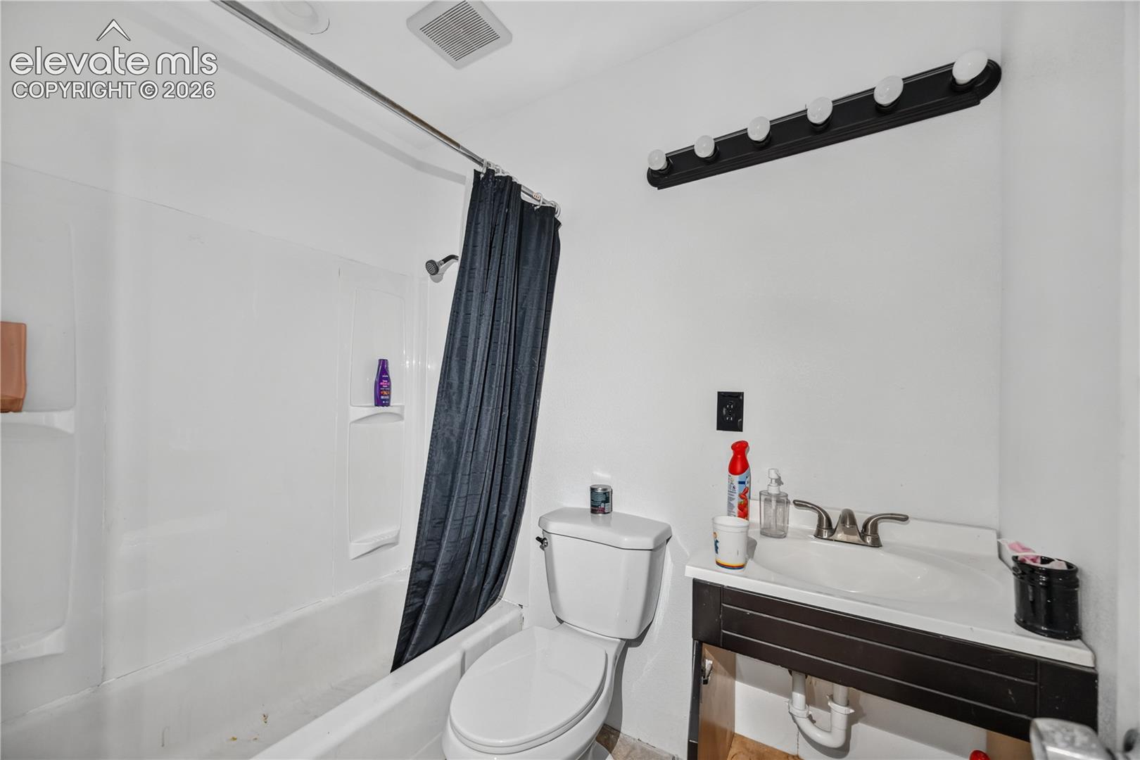 Bathroom featuring a combination bathtub and shower with a white surround, vanity with a rectangular basin and metal faucet, and a wall-mounted light fixture