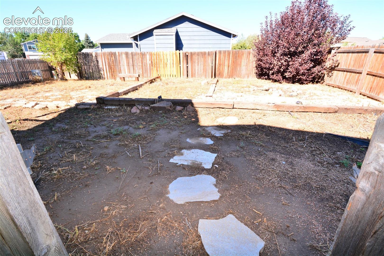 Enclosed backyard space featuring a wooden privacy fence, stone pathway, and defined garden beds