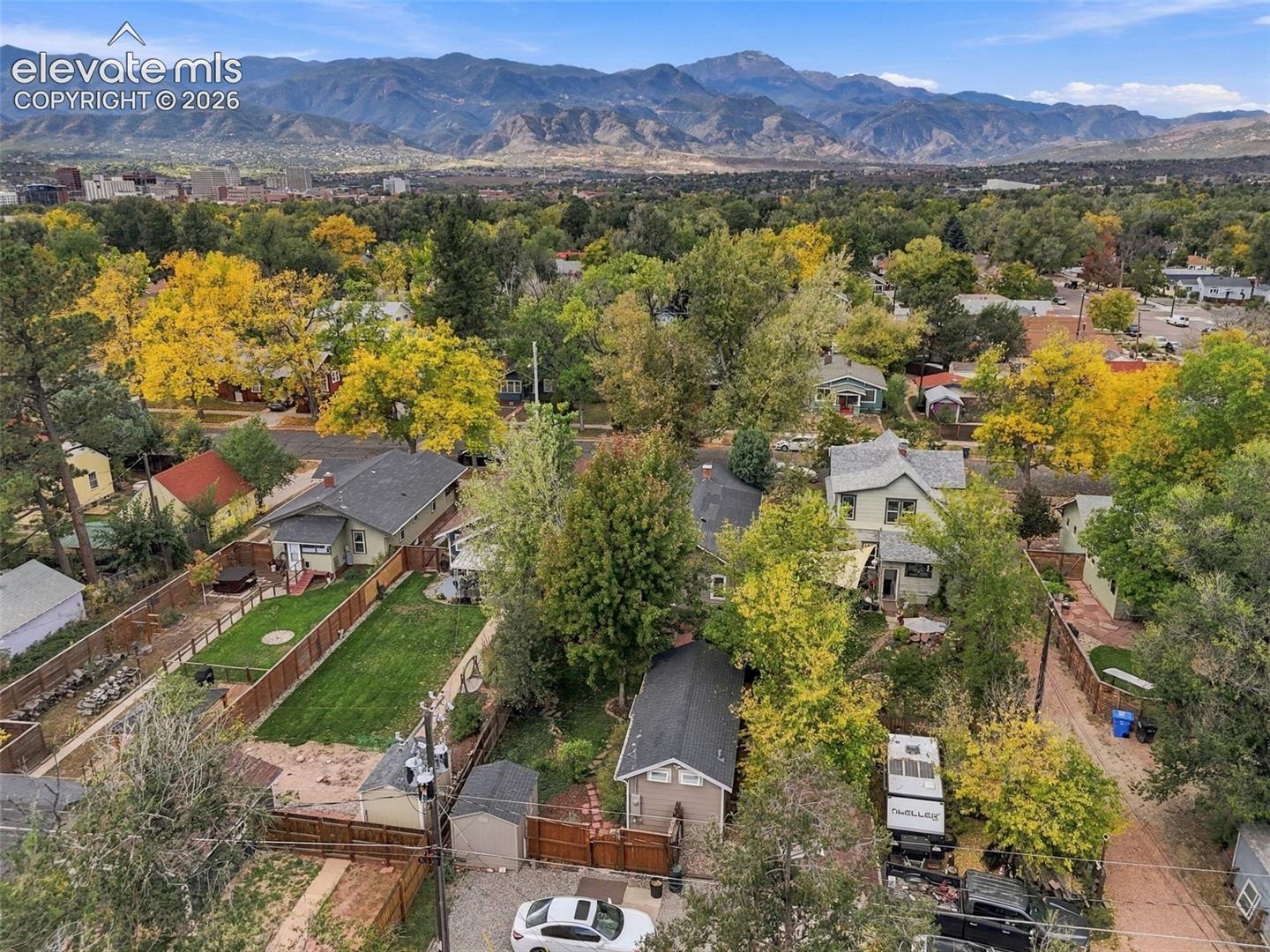 Aerial perspective showcasing a residential lot featuring a manicured lawn, wood fencing, detached storage structure, and a mountain range backdrop