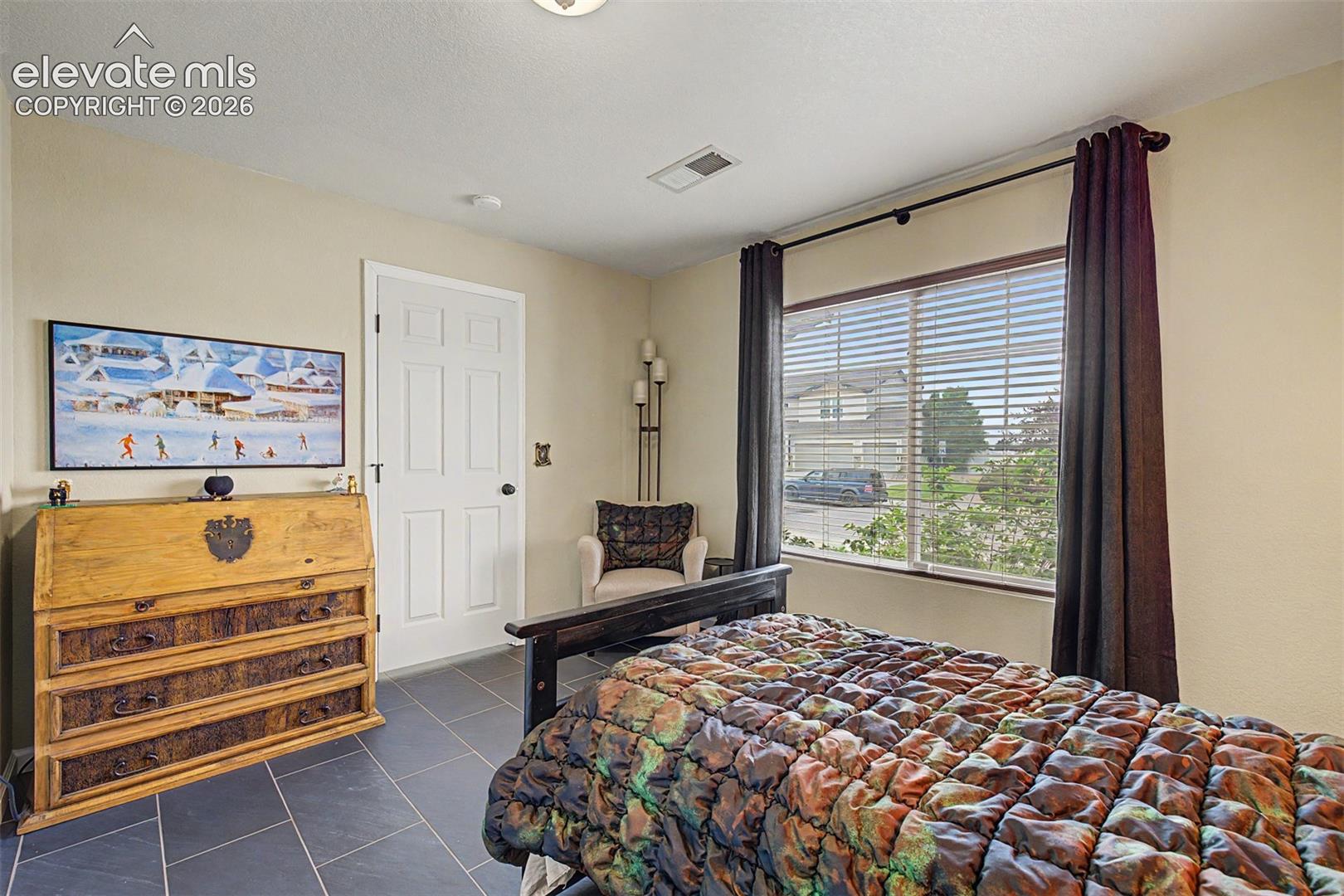 Warm tones, dark tile flooring, and a large window give this bedroom a cozy, cabin-inspired character — a room that feels like it belongs somewhere special.