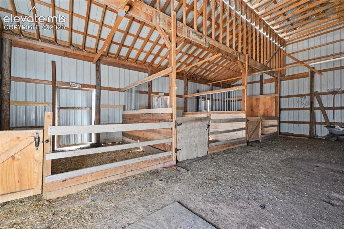 Multi-stall barn interior featuring exposed wood post-and-beam construction, wood-plank dividers, metal siding, and open rafter ceiling