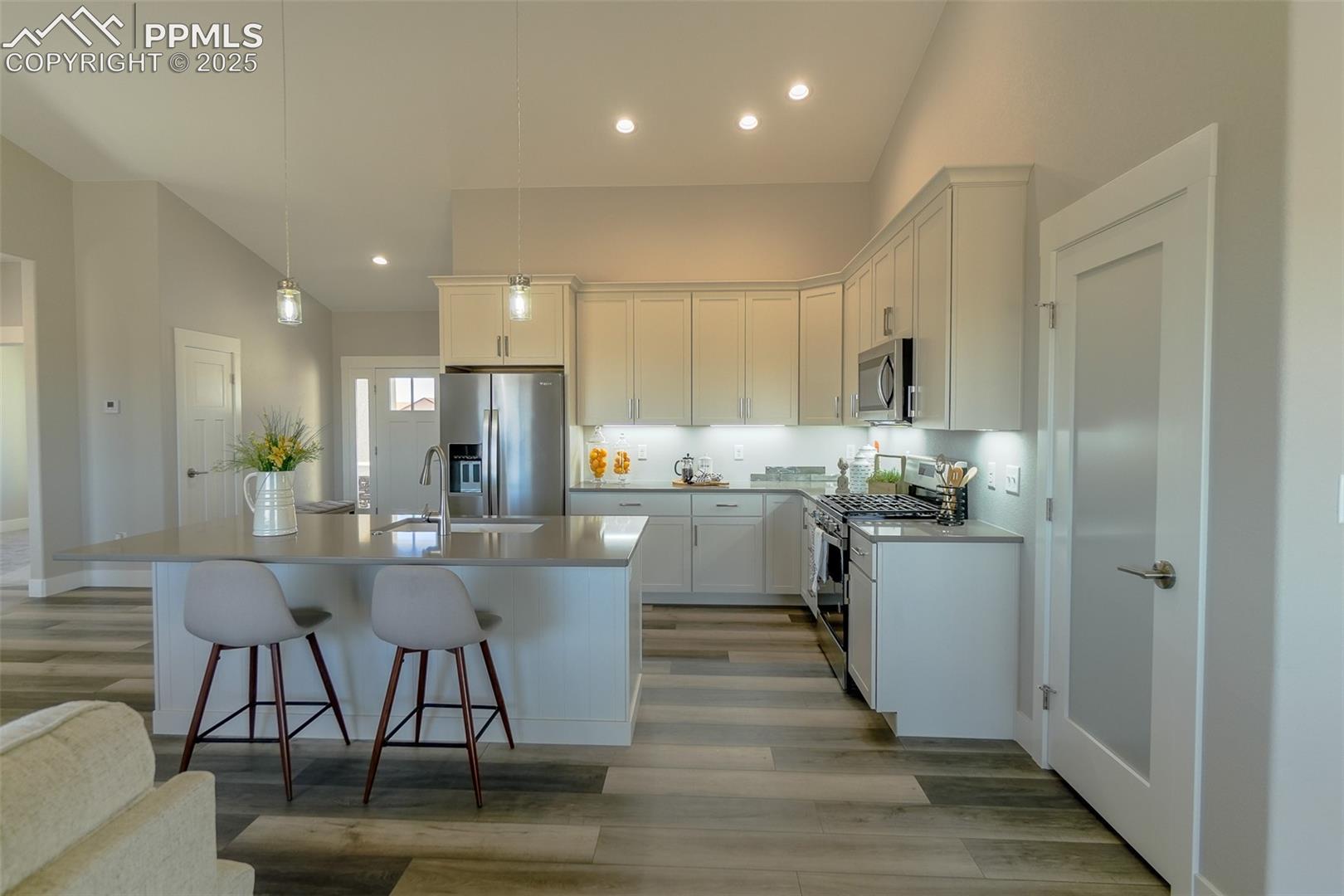 Kitchen with sink, appliances with stainless steel finishes, light wood-LTV flooring, and an island with sink