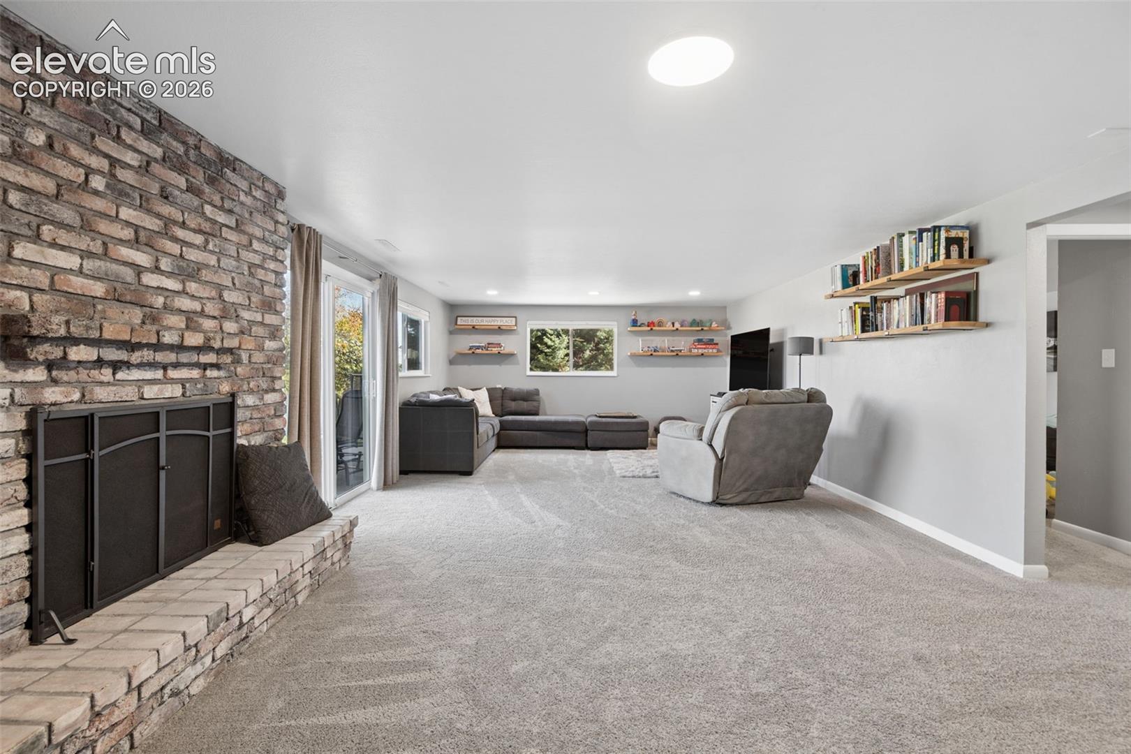 Basement Living area featuring a floor-to-ceiling brick fireplace with a raised brick hearth, recessed lighting, and wall-mounted floating shelving