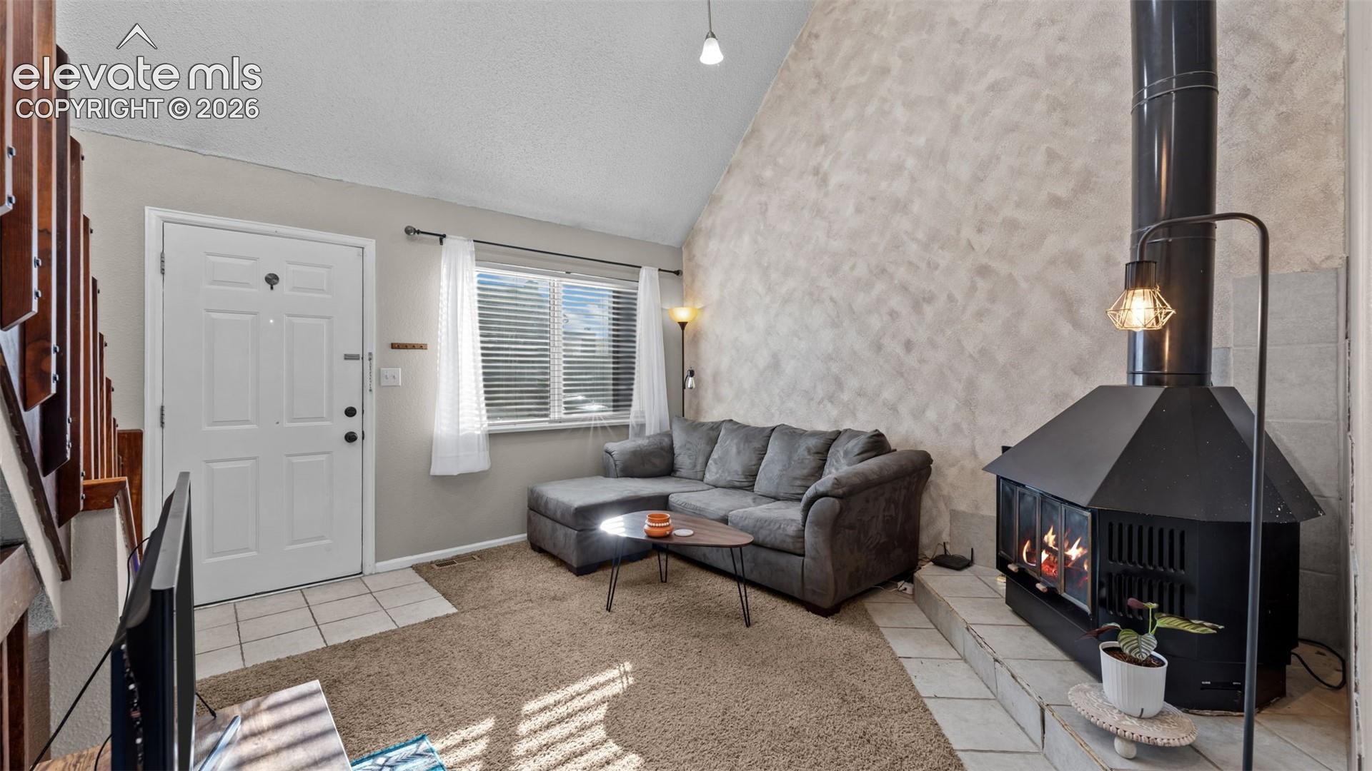 Vaulted ceilings, textured wall finish, and a black metal freestanding fireplace on a raised tiled hearth