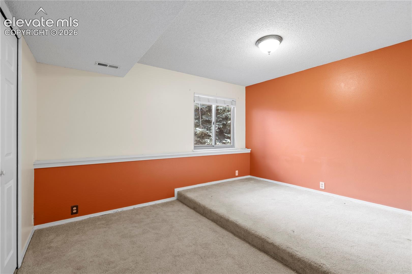 Recessed window, two-tone wall treatment, built-in elevated platform, wall-mounted lighting fixture, and carpet flooring