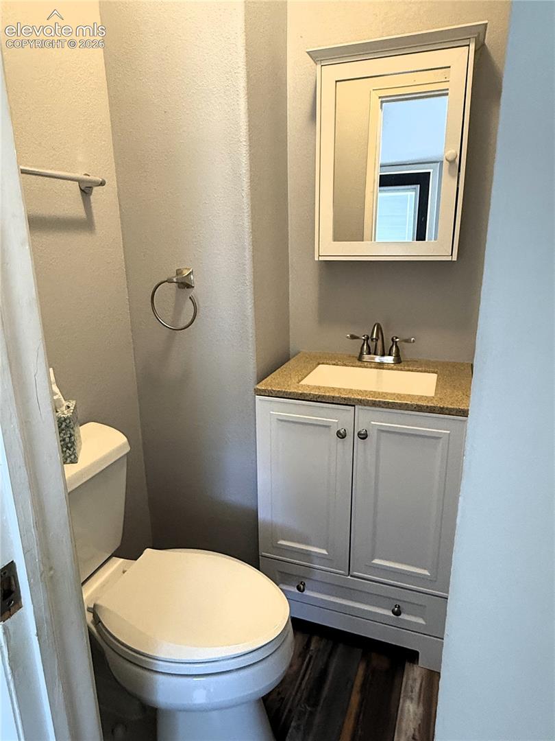 White vanity with a neutral stone-finish countertop, integrated basin, wall-mounted medicine cabinet, and wood-finish flooring