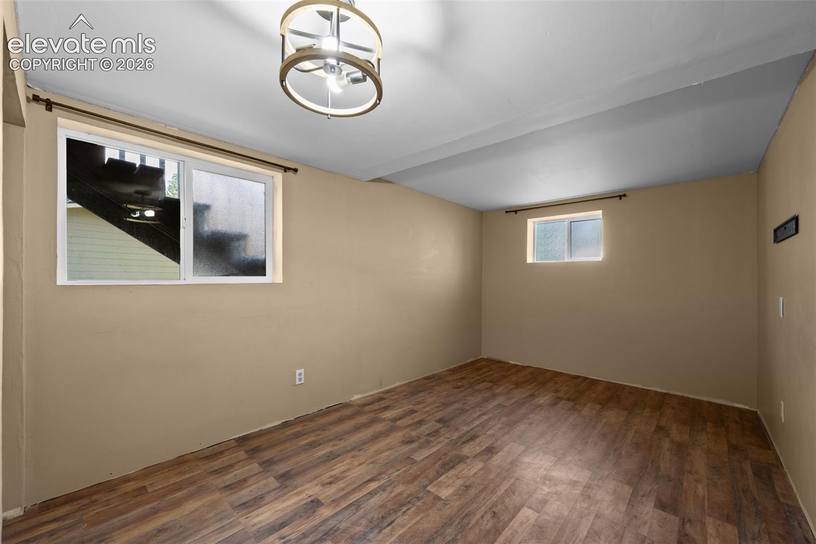 Interior room featuring wood-finish flooring, a drum-style pendant light fixture, and two horizontal slider windows