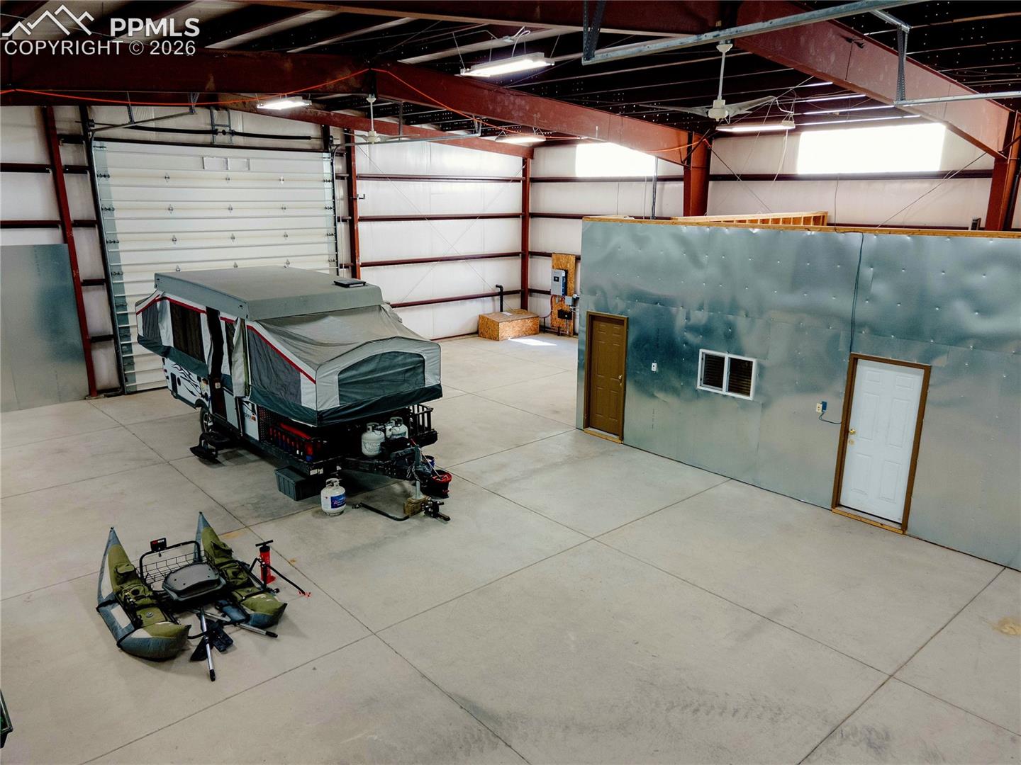 Spacious warehouse interior featuring a large roll-up door, exposed metal beam construction, and a concrete floor