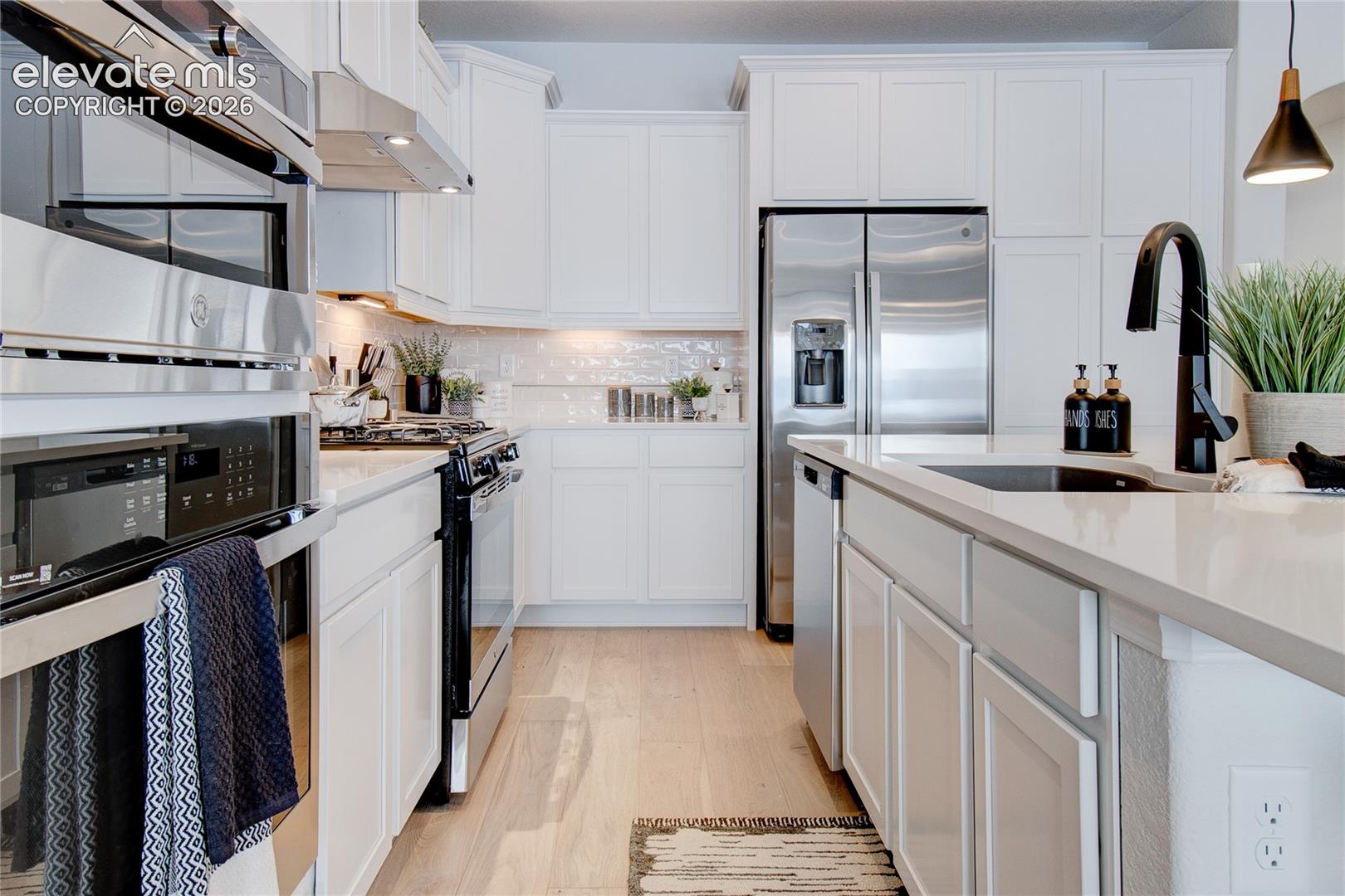 Kitchen featuring white shaker-style cabinetry, stainless steel appliances, light-toned wood-finish flooring, stone-composite countertops, and a matte black gooseneck faucet