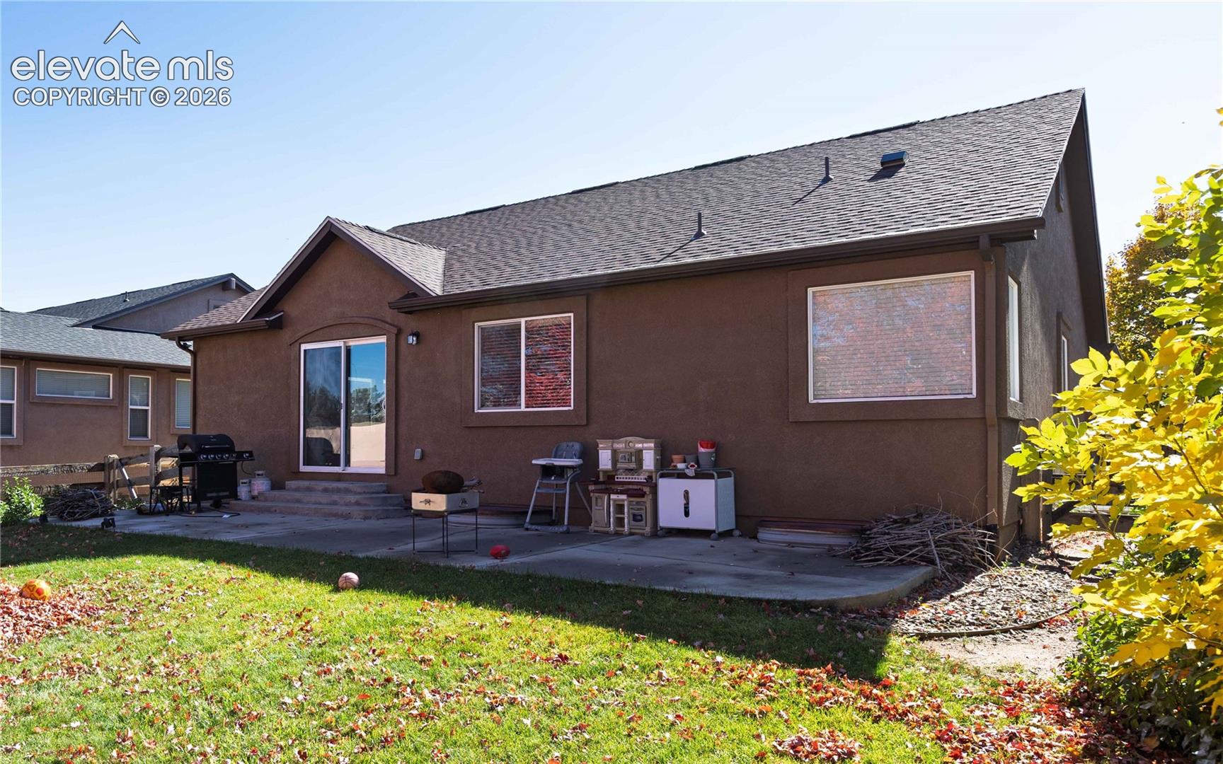 Stucco exterior with asphalt shingle roof, concrete patio, and sliding glass door