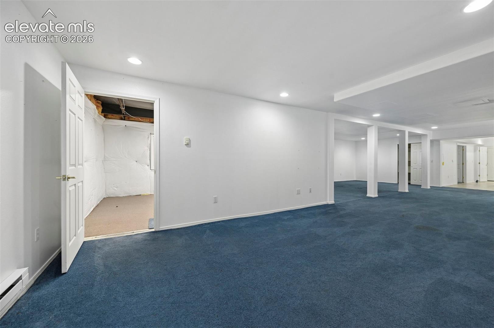 Expansive carpeted area with recessed lighting, structural support columns, and white painted walls
