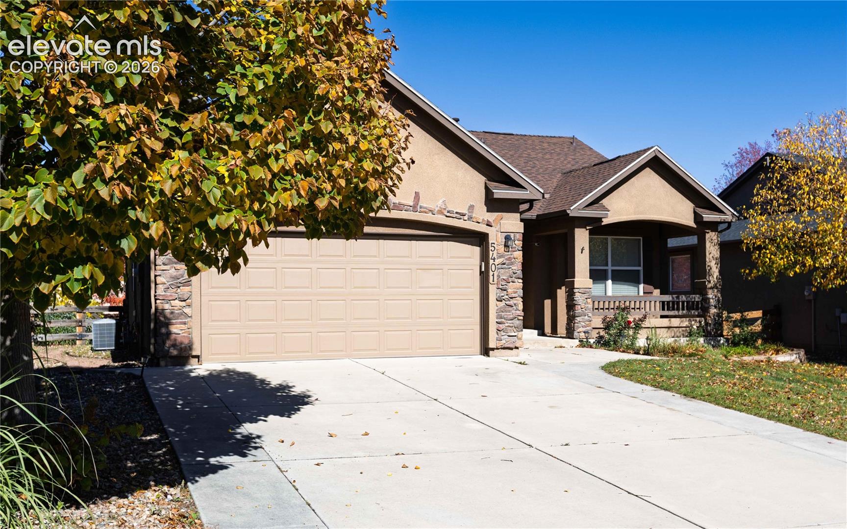 Stucco and stone veneer exterior featuring a two-car garage, covered front porch, and shingle roofing