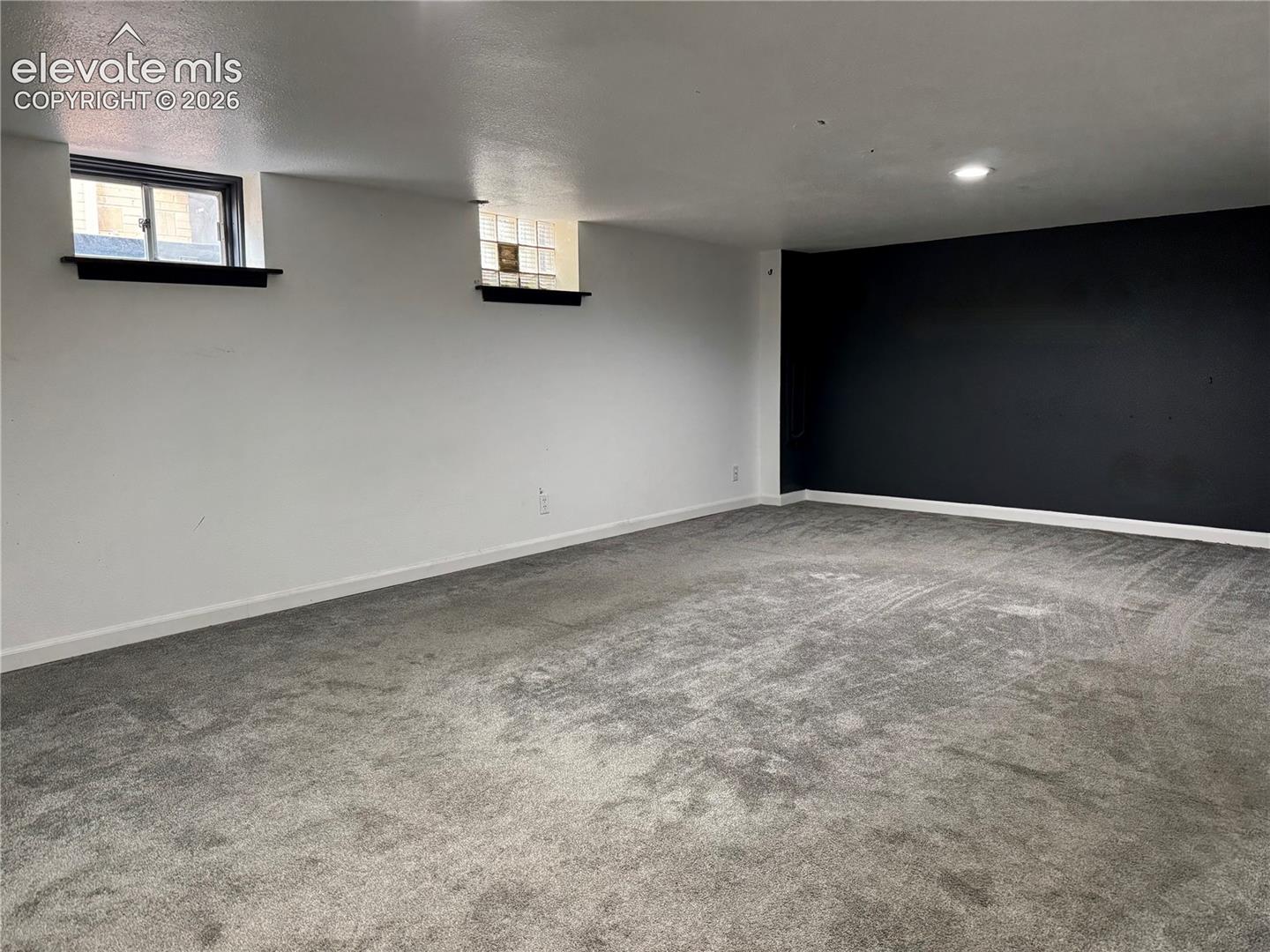 Neutral-toned wall-to-wall carpeting, high-contrast accent wall, recessed lighting, and dual inset windows