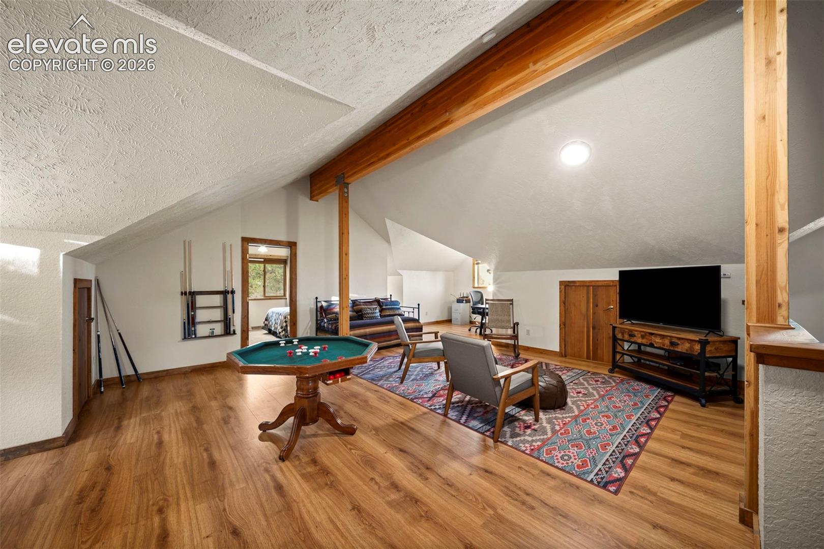 Vaulted ceiling featuring exposed wood support beams, wood-finish flooring, and built-in wall cabinetry