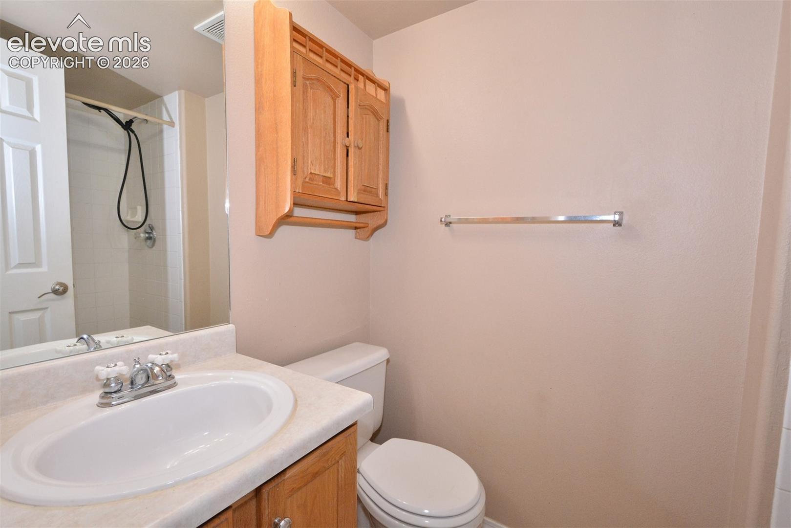 Wood-finish cabinetry, built-in medicine cabinet, white drop-in sink, shower enclosure, and white toilet