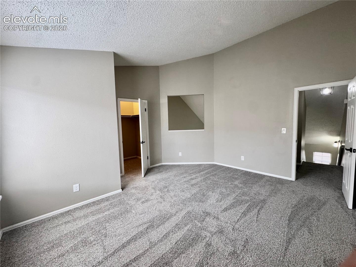 Vaulted ceiling, neutral wall paint, gray carpeting, and a built-in wall niche