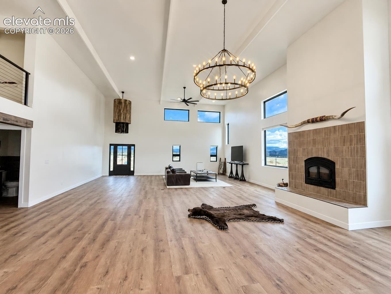 Expansive room with high vaulted ceilings, wood-finish flooring, multi-tier circular chandelier, and a floor-to-ceiling fireplace featuring vertical tile surround