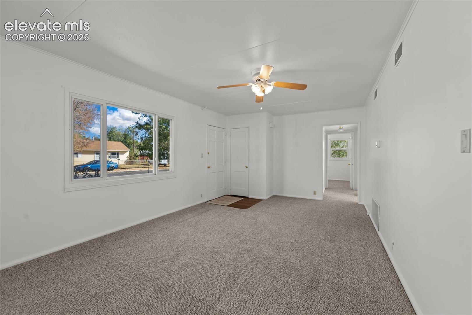 Living area featuring neutral carpeting, a large picture window, and a central ceiling fan with integrated light fixture