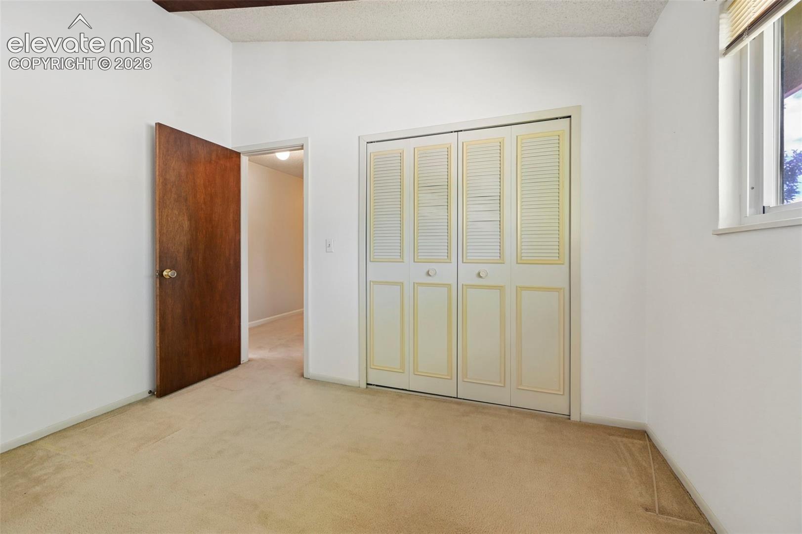 Carpeted flooring, white walls, wood-finish interior door, bifold closet doors, and window with blinds