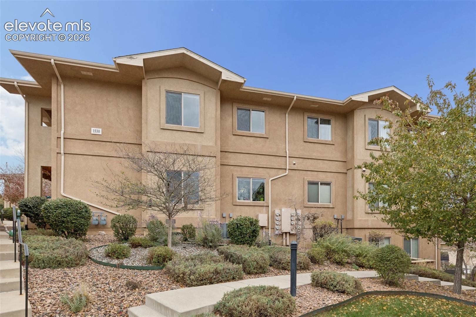 Stucco exterior featuring multi-level rooflines, single-hung windows, and a paved concrete walkway surrounded by xeriscaped landscaping
