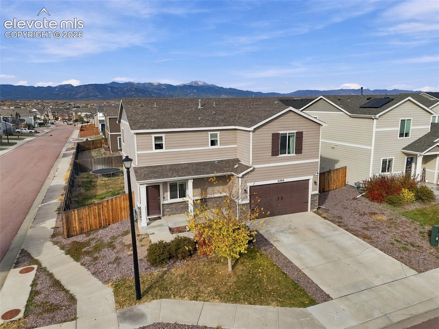 Two-story residence featuring horizontal siding, stone veneer accents, an attached two-car garage, concrete driveway, and mountain scenery