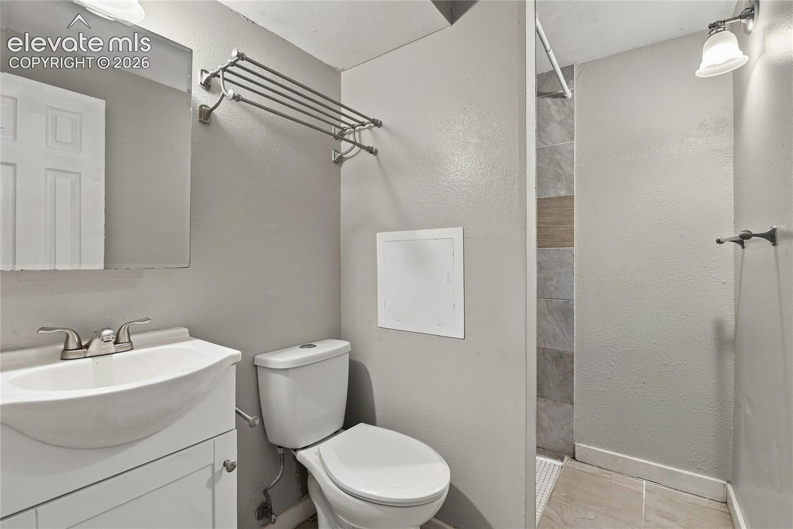 Basement bathroom featuring a curved pedestal sink with chrome faucet and vanity storage, a white ceramic toilet with elongated bowl, tile flooring, recessed lighting, and a walk-in shower with tile surround