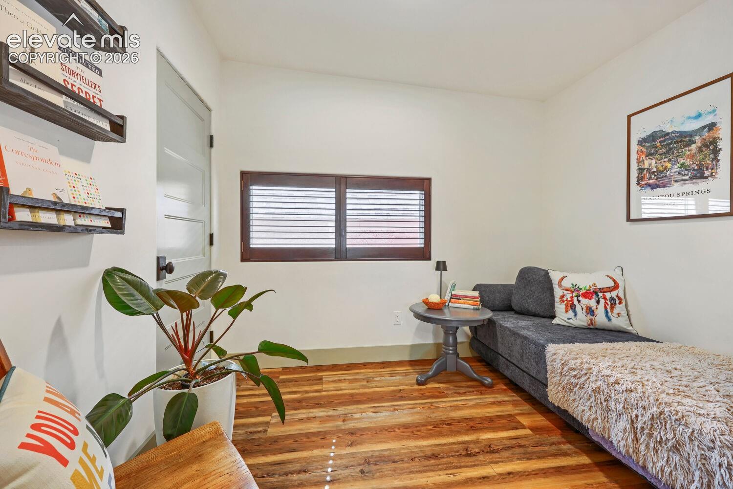 Wood-finish flooring, white walls, and a window with wood shutters