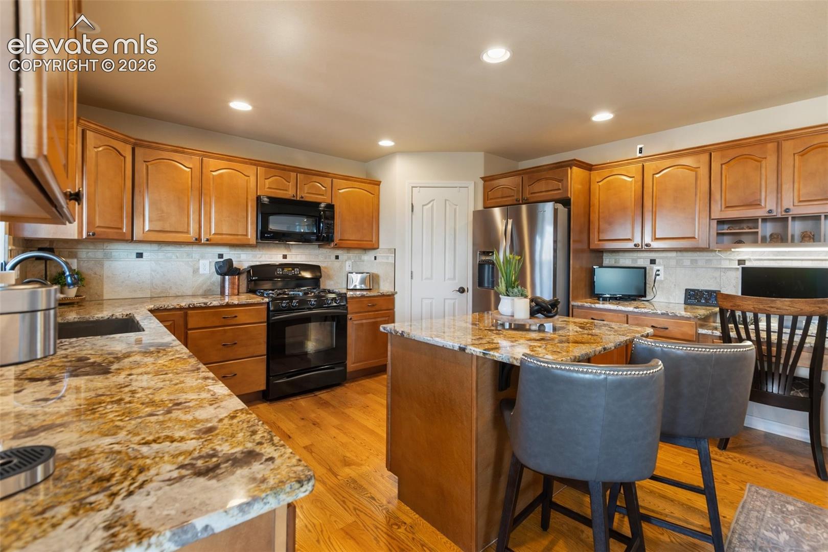 Kitchen featuring stone countertops, stained wood cabinetry, stainless steel appliances, a central island, and wood-finish flooring