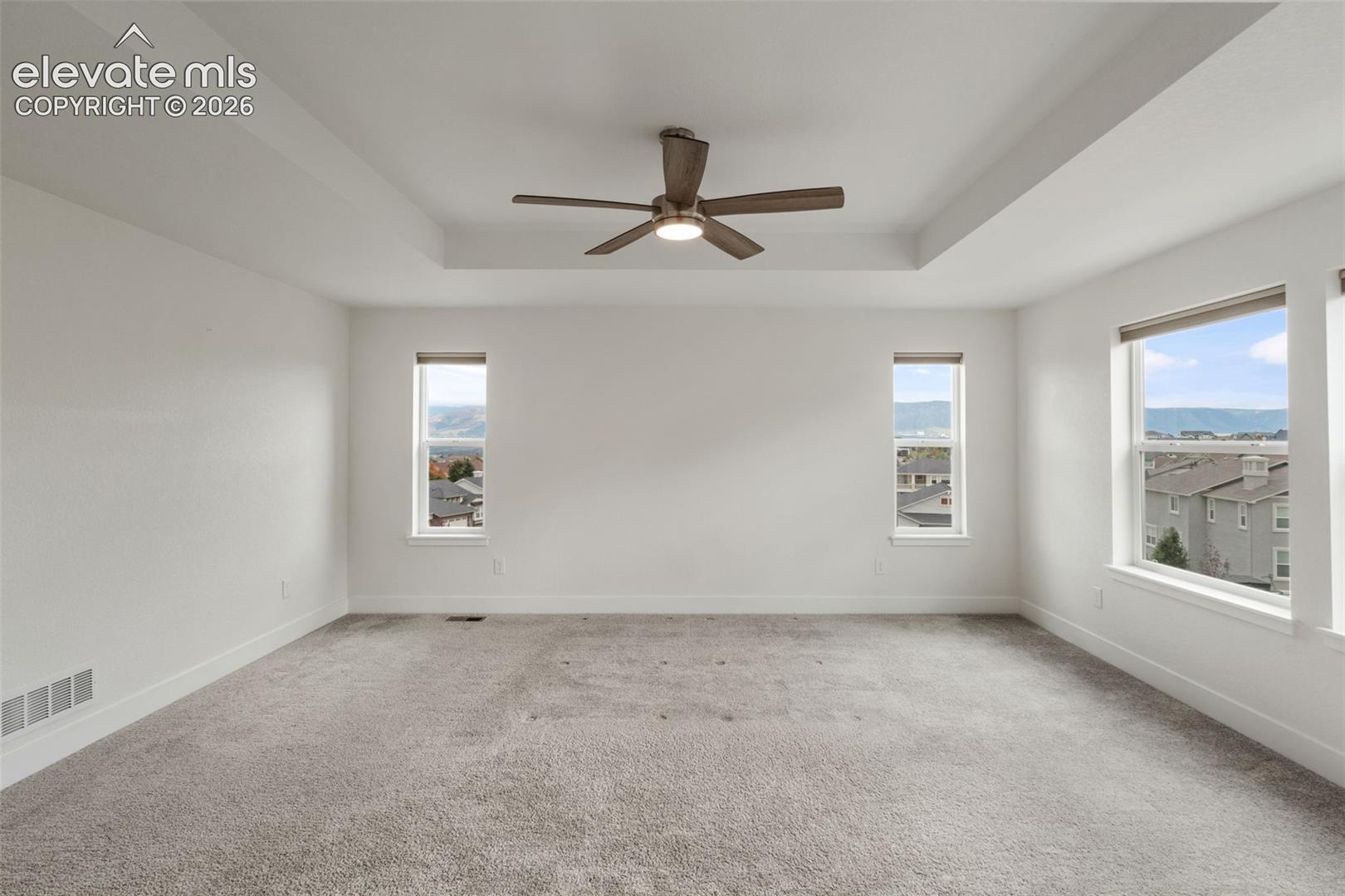 Tray ceiling with a ceiling fan, plush carpeting, and spectacular mountain views